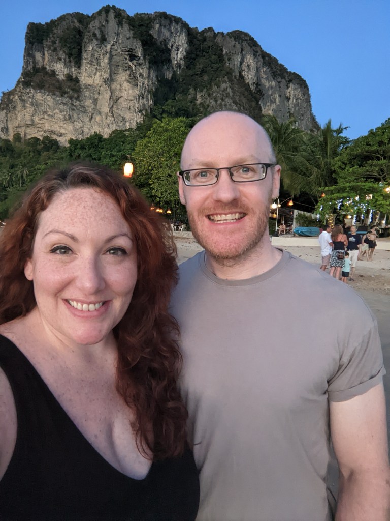 Photo of man and woman smiling in front of mountain on the beach.