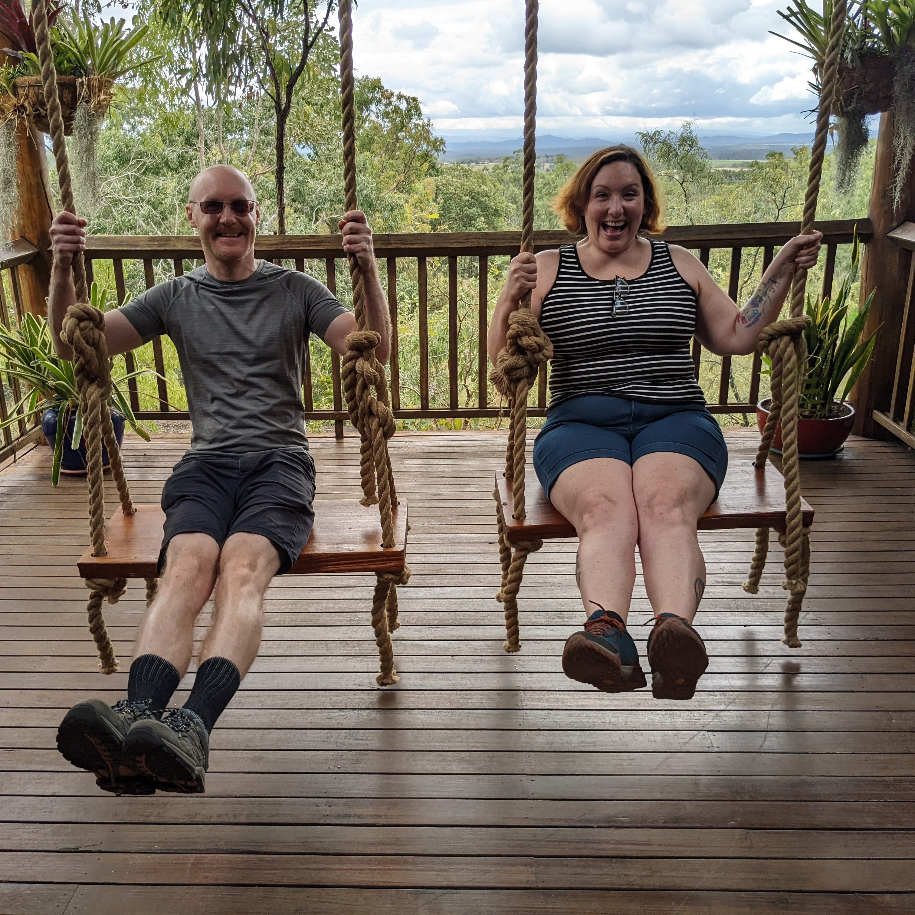 A man and a woman sitting on wooden swings on a wooden porch. 